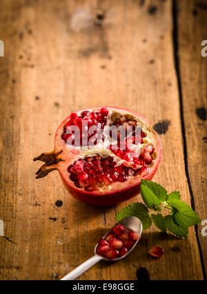 Dimezzato il melograno fresco con i semi in un cucchiaino di ricco in vitamine e utilizzato in medicina ayurvedica su una tavola in legno rustico con Foto Stock