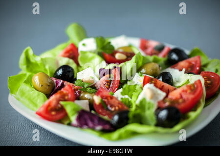 Basso angolo vista di una piastra di fresco e salutare insalata mediterranea con feta, pomodoro e olive su un letto di foglie verdi Foto Stock