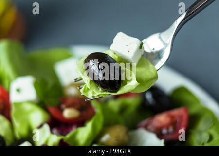 Mangiare un misto di insalata greca con un nero oliva, il formaggio feta e lattuga su una forcella sopra un piatto di insalata con la messa a fuoco a forcella Foto Stock