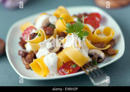 Ampia pappardelle ribbon Pasta con funghi, pomodori e una saporita salsa di panna e guarnita con prezzemolo servite su un piatto da portata Foto Stock