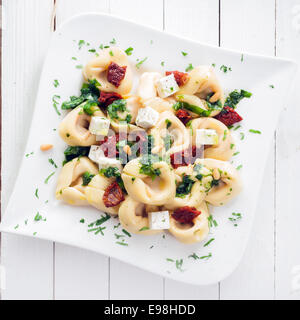 Vista in pianta di una piastra di insaccati tortellini italiana la pasta con il formaggio feta e pesto cosparso con erbe fresche e pinoli Foto Stock