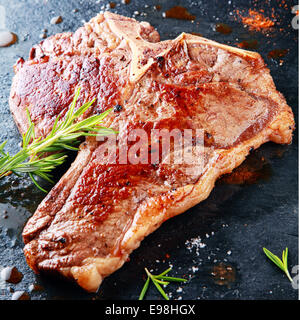 Deliziose grigliate di t-bone steak su una piastra calda condita con rosmarino fresco, le erbe aromatiche e le spezie in una Steakhouse o ristorante Foto Stock