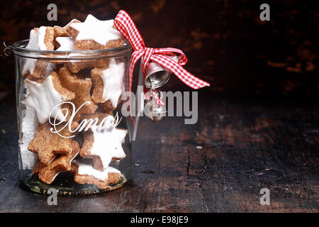 Gustosi biscotti di Natale nel recipiente trasparente con argento campane, isolato su Vintage sfondo tabella. Foto Stock