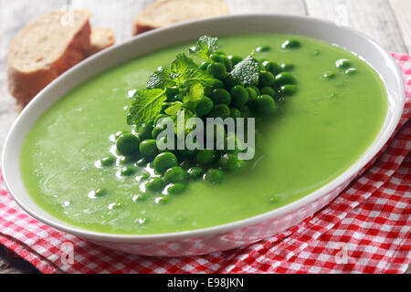 Sana Gourmet verde zuppa di piselli piatto su bianco ciotola poco profonda posto sopra a quadretti rossi telo bianco al tavolo di legno. Foto Stock