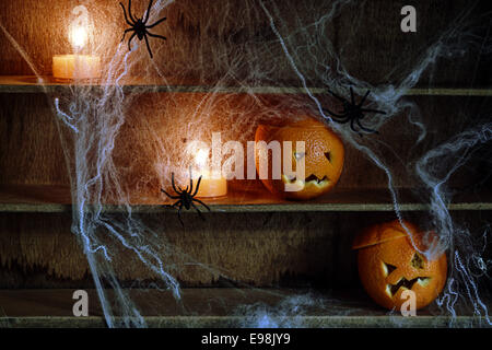 Due Halloween Jack o lanterne intagliati da arance e Spiderwebs con ragni e candele accese sugli scaffali Foto Stock