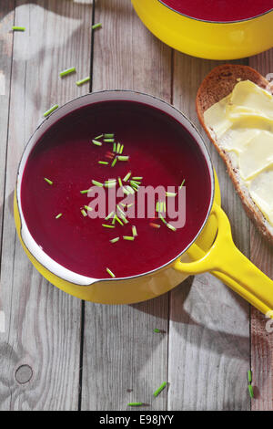 Rosso violetto zuppa di barbabietole in giallo Pot, perfetto per pane con diffusione, posto su Vintage tavolo in legno. Foto Stock