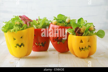 Colorate il cibo di Halloween con sfondo colorato farcite sani di rosso e di giallo dolci peperoni con facce di esclusione nella pelle come halloween jack-o-lanterne riempito con insalata verde e formaggio Foto Stock