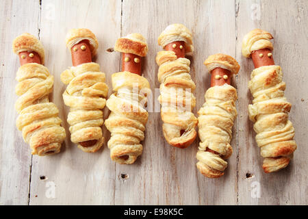 Sei Weiners avvolto in pasticceria a guardare come mummie di Halloween su sfondo di legno Foto Stock