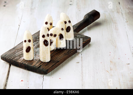 Banana fantasmi di Halloween con facce di cioccolato sul tagliere di legno Foto Stock