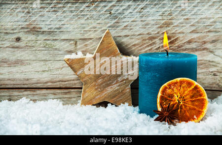 Paese natale sfondo con una candela che brucia e lavorati a mano la stella di  legno in piedi nella neve invernale con un essiccato fetta di arancia  contro il vecchio di tavole di legno con copyspace Foto stock - Alamy