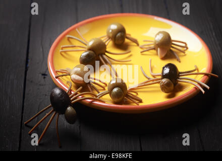 Scary Halloween spider antipasti indurito con olive nere e verdi con spaghetti gambe strisciando su una piastra di colore giallo su un buffet contro uno sfondo scuro Foto Stock