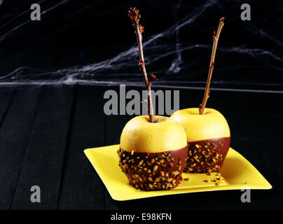 Un sano Halloween dessert apple con una coppia di freschi mele golden immersi nel cioccolato e spruzza decorata con ramoscelli drappeggiati in ragnatele su sfondo scuro con copyspace Foto Stock