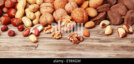 Varietà di sgusciate e frutti a guscio interi in un banner orizzontale tra cui mandorle, nocciole, noci del Brasile, arachidi e le noci su un rustico in legno con sfondo copyspace Foto Stock