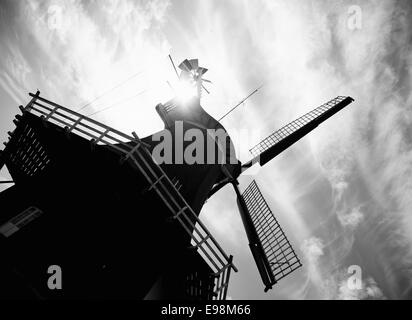 Immagine in bianco e nero di un mulino a vento inclinato con esso vele e balcone stagliano contro un cielo nuvoloso da una svasatura di Sun al di sopra del tetto. Foto Stock