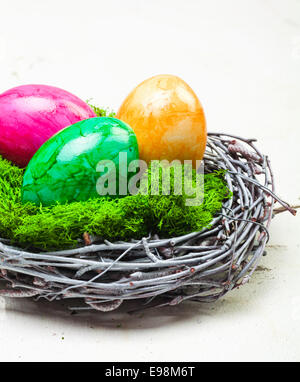Tre in marmo colorato le uova di Pasqua su muschio verde in un nido costruito di ramoscelli intrecciati Foto Stock