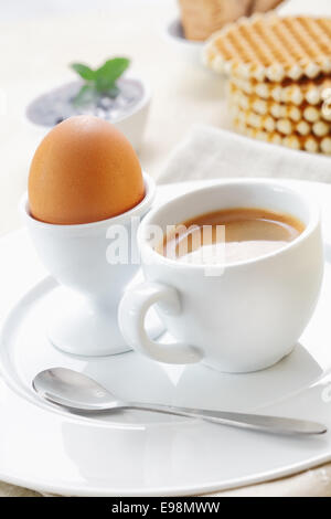 Recentemente bollita uovo marrone in un eggcup servita su una piastra con una tazza di caffè forte caffè per la prima colazione Foto Stock