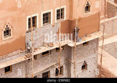 Lavoratori applicando tradizionale rosso intonacatura di argilla ad un edificio, su impalcature in legno nel deserto città di Ouarzazate, Marocco Foto Stock