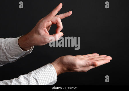 Maschio caucasico mani sparare via qualcosa davanti a uno sfondo nero Foto Stock