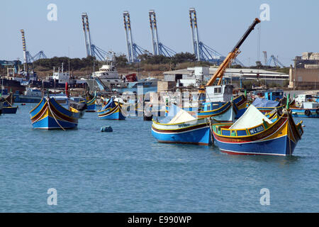 Pesche barca nel porto di Marsaxlokk con le gru di Malta Freeport terminal per container in background, Malta Foto Stock