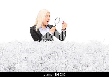 Scioccato donna che guarda ad una pila di carta tagliuzzata attraverso una lente di ingrandimento isolati su sfondo bianco Foto Stock