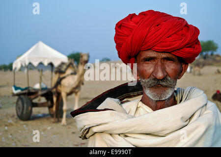 Ritratto di un uomo vecchio con il camel carrello in background, Pushkar, Ajmer, Rajasthan, India Foto Stock