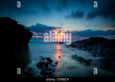 Nuvoloso Tramonto su scogli lungo la costa della Cornovaglia vicino a Newquay, Cornwall, Inghilterra Foto Stock