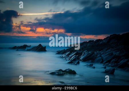 Nuvoloso Tramonto su scogli lungo la costa della Cornovaglia vicino a Newquay, Cornwall, Inghilterra Foto Stock