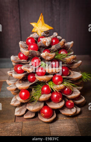 Pigna decorata con mirtilli rossi come albero di natale su sfondo in legno decorazioni di Natale di pigne e bacche Foto Stock