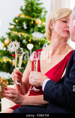 Senior l uomo e la donna che celebra la vigilia di Natale con i Kiss e vino spumante Foto Stock