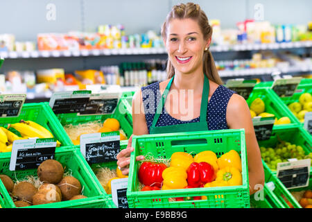 Organico femmina il negozio di drogheria assistant riempimento noci di cocco i rack di stoccaggio nel dipartimento di vegetali Foto Stock