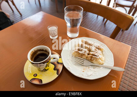 Stilllife di pasta (Baklava) sulla piastra, una tazza di caffè greco un bicchiere di acqua e il progetto di legge in un vetro, isola di Kos, Grecia Foto Stock