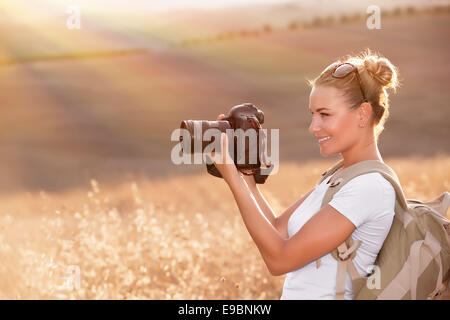 Felice fotografo godere la natura in autunno e sorridente ragazza di viaggiatori con la fotocamera in mano a fotografare golden dry campo di grano Foto Stock