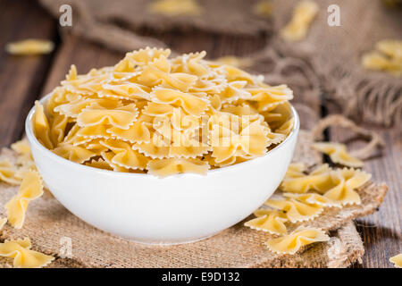 Farfalle (comunemente noto come pasta Bow-Tie) in una ciotola su sfondo di legno Foto Stock