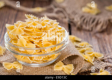 Farfalle (comunemente noto come pasta Bow-Tie) in una ciotola su sfondo di legno Foto Stock