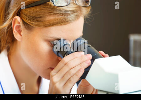 Bella donna in un laboratorio lavora con un microscopio. Foto Stock