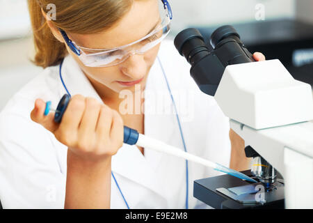 Bella donna in un laboratorio lavora con un microscopio. Foto Stock