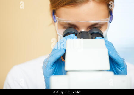 Bella donna in un laboratorio lavora con un microscopio. Foto Stock