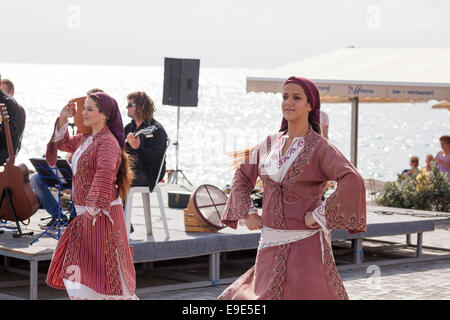 Paphos, Cipro - 24 Novembre 2013 due giovani donne nei tradizionali costumi cipriota a ballare la musica dal vivo sul lungomare. Foto Stock