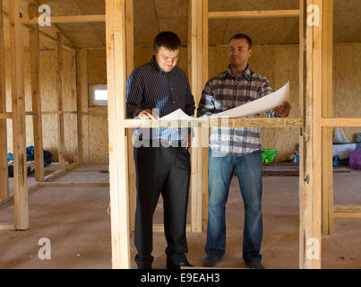 Due architetti o costruttori consulting piani in una metà costruito casa con struttura in legno Foto Stock