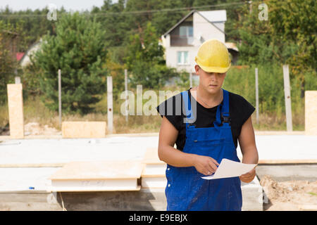 Costruttori specifiche di controllo o un ordine di materiali da costruzione come egli si trova sul sito nella sua hardhat e tute da lavoro Foto Stock