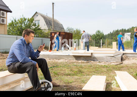 Sito maschio ingegnere occupato di messaggistica utilizzando il suo telefono cellulare presso l'Area di progetto. Foto Stock