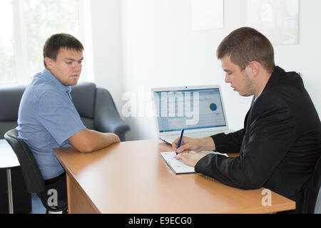 Seri uomini d'affari in ufficio in legno scrivania con computer portatile osservando qualcosa sul notebook. Foto Stock