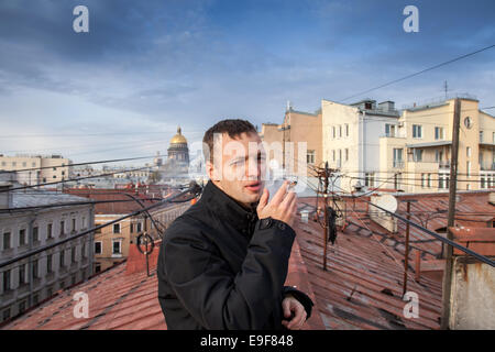 Giovane uomo caucasico fuma sigaro sul tetto nella parte centrale di San Pietroburgo, Russia Foto Stock