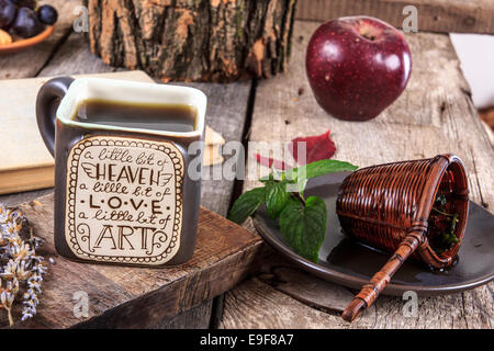 Close up di interessanti tazza di tè con un messaggio su un tavolo di legno con un colino su una piastra accanto alla tazza e aprire vecchio libro, autu Foto Stock