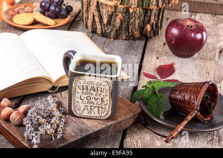 Interessante tazza di tè con un messaggio su un tavolo di legno con un colino su una piastra accanto alla tazza e aprire vecchio libro, autunno decoratio Foto Stock