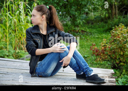 La ragazza seduta su assi di legno in un giardino estivo Foto Stock