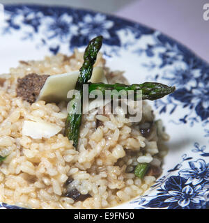 Alta fine food, rissoto Riso con funghi porcini servito con le fette di formaggio sulla parte superiore e gli asparagi in un art deco piastra blu, Foto Stock