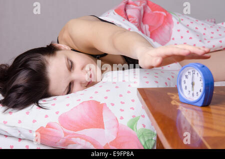 La donna dorme nel letto, in piedi accanto a una sveglia sul tavolo, i luoghi sull'ore sei Foto Stock