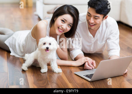 Coppia giovane sdraiato sul pavimento con il laptop con un simpatico cane Foto Stock