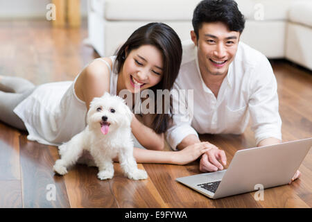 Coppia giovane sdraiato sul pavimento con il laptop con un simpatico cane Foto Stock